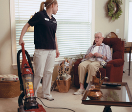 A person holding a vacuum cleaner and talking to an elderly person