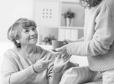 A person giving a cup to an elderly person sitting on the sofa